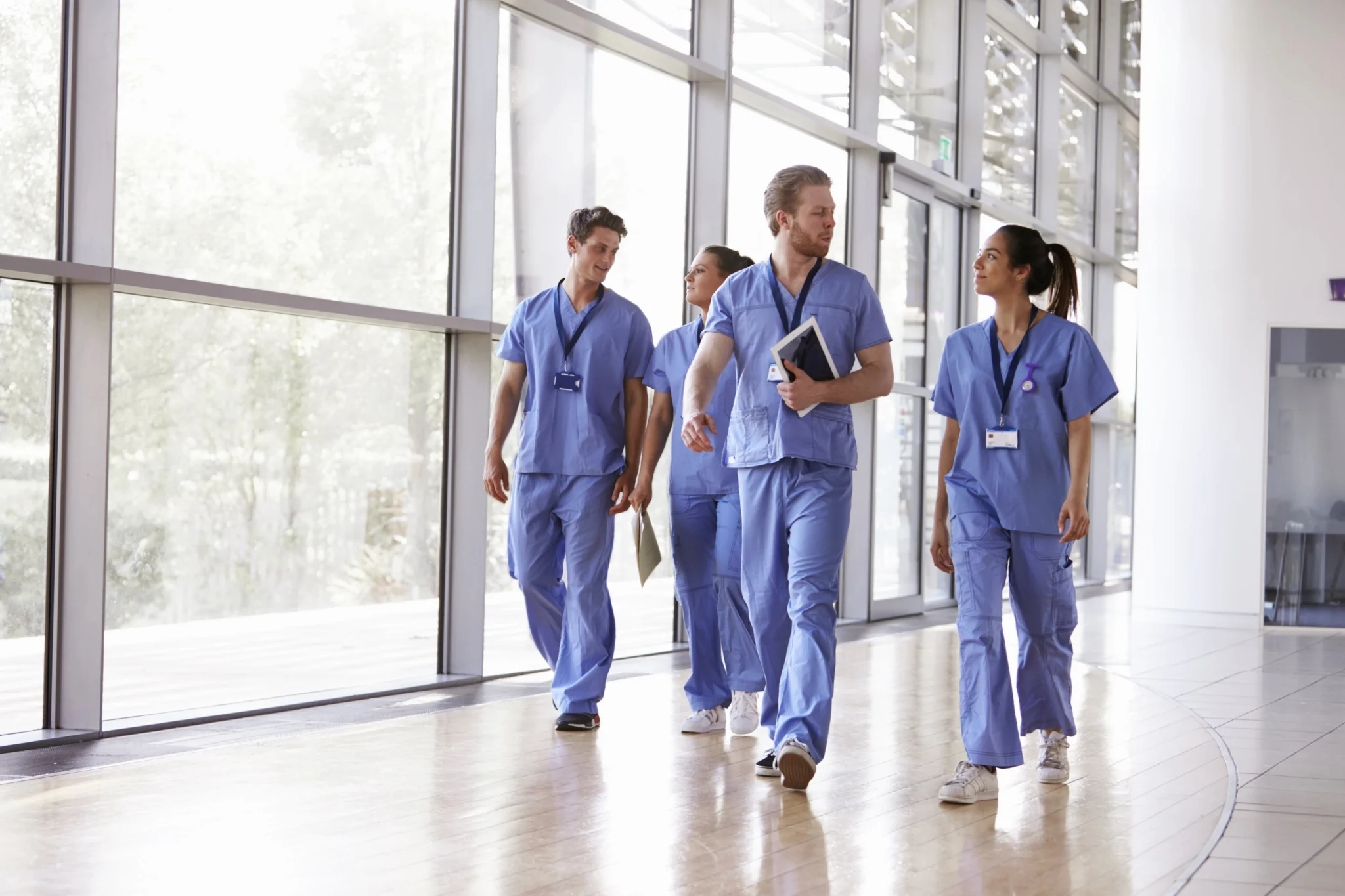 Four healthcare workers in scrubs walking down a clinic corridor